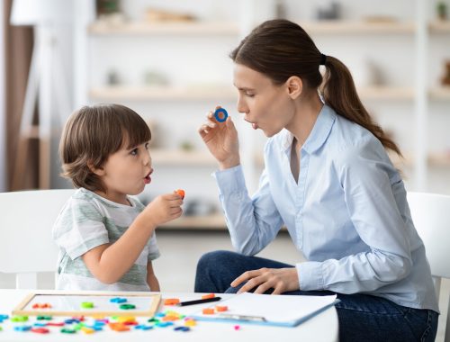 Female speech therapist curing child's problems and impediments. Little boy learning letter O with private English language tutor during lesson at office